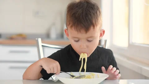 Child 6 years old boy in the kitchen eating pasta Stock Footage 144193239
