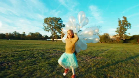 Child 8-9 years old running across field at sun in sunset with balloons Stock Footage 67684677