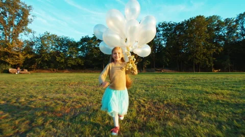 Child 8-9 years old running at camera and holds her white balloons and smiling Stock Footage 67685025