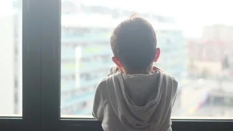 Child alone in front of a large window with his back to himself. Video stock 270461358