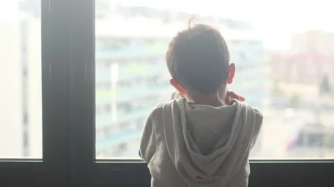 Child alone in front of a large window with his back to himself. Video stock 270461373