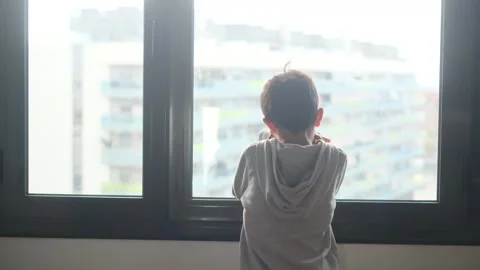 Child alone in front of a large window with his back to himself. Video stock 270461381