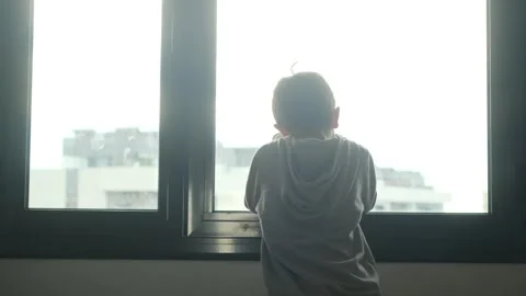 Child alone in front of a large window with his back to himself. Video stock 270461383
