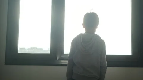 Child alone in front of a large window with his back to himself. Video stock 270461390