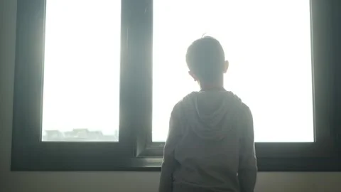 Child alone in front of a large window with his back to himself. Video stock 270461399