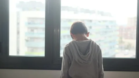 Child alone in front of a large window with his back to himself. Video stock 270461417