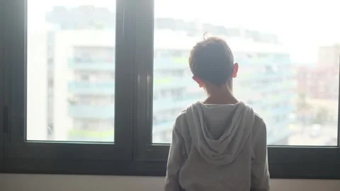 Child alone in front of a large window with his back to himself. Video stock 270461419