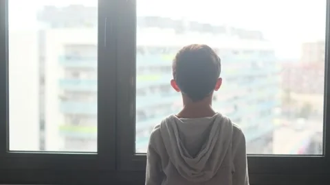 Child alone in front of a large window with his back to himself. Video stock 270461430