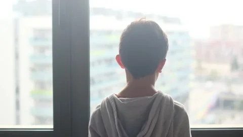 Child alone in front of a large window with his back to himself. Video stock 270461436
