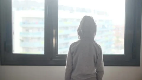Child alone in front of a large window with his back to himself. Video stock 270461443