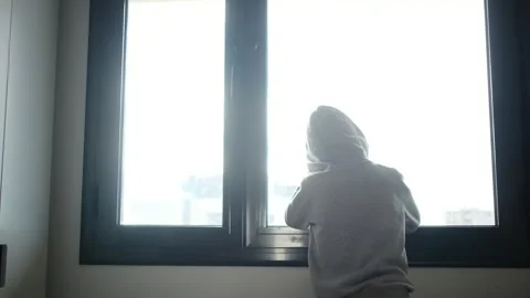 Child alone in front of a large window with his back to himself. Video stock 270461496