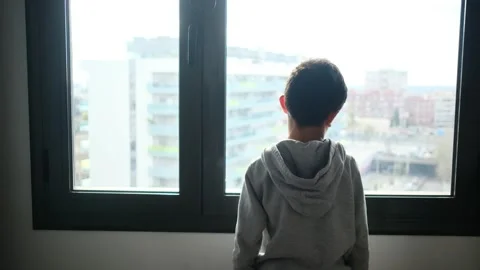 Child alone in front of a large window with his back to himself. Video stock 270461542