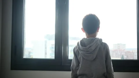 Child alone in front of a large window with his back to himself. Video stock 270461555
