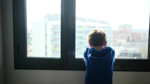 Child alone in front of a large window with his back to himself. Video stock 270461556