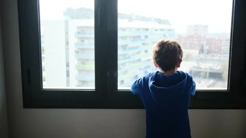 Child alone in front of a large window with his back to himself. Video stock 270461565