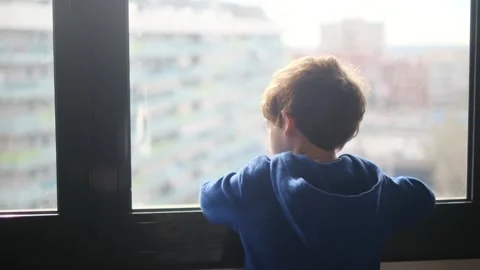Child alone in front of a large window with his back to himself. Video stock 270461583