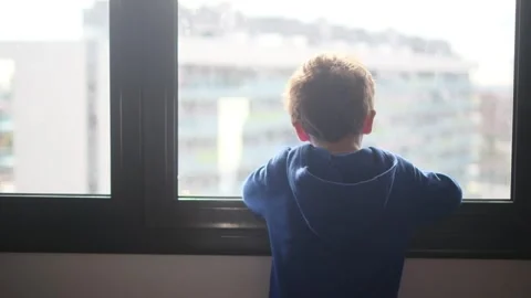 Child alone in front of a large window with his back to himself. Video stock 270461585
