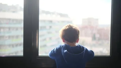 Child alone in front of a large window with his back to himself. Video stock 270461592