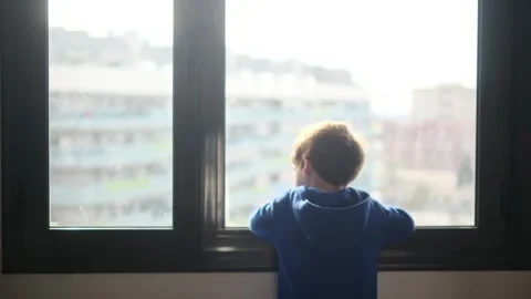 Child alone in front of a large window with his back to himself. Video stock 270461596