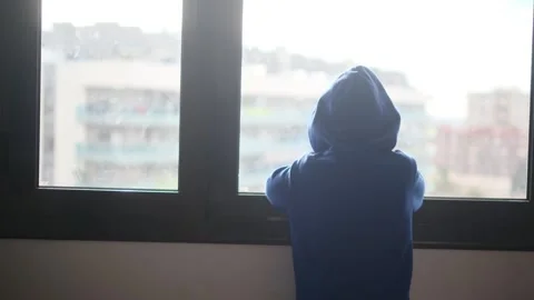 Child alone in front of a large window with his back to himself. Video stock 270461609