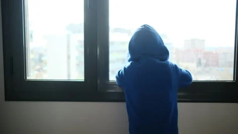 Child alone in front of a large window with his back to himself. Vídeos de archivo 270461618