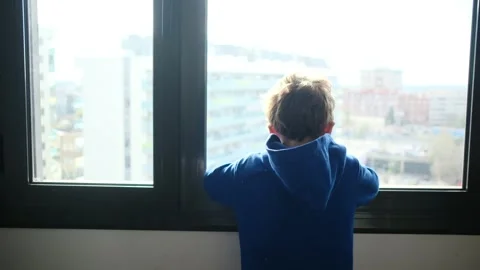 Child alone in front of a large window with his back to himself. Video stock 270461623