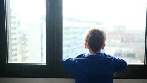 Child alone in front of a large window with his back to himself. Vídeos de archivo 270461629
