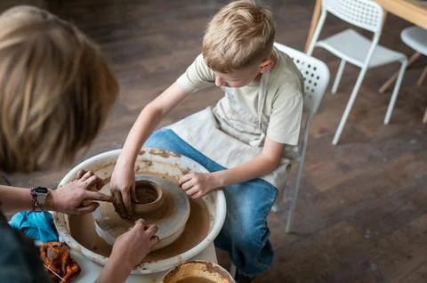 Child and instructor shaping clay together at pottery workshop Stock Photos
