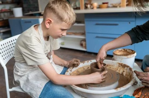 Child and instructor shaping clay together at pottery workshop Stock Photos