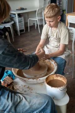 Child and instructor shaping clay together at pottery workshop Stock Photos