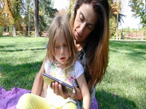 Child and mother talking watching smartphone in park Stock Footage 80422250