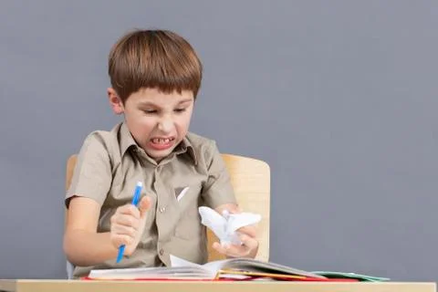 The child is angry at homework. An elementary school student is tearing paper. Fotos de archivo