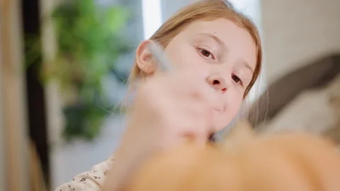 Child artist carefully paints pumpkin in cozy setting. Playful young girl Stock Footage 346390553