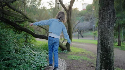 Child Balancing on Fallen Tree Log in Green Park with Arms Outstretched. Stock-Footage 338140379