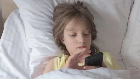 Child in bed using phone, covered with white blankets Stock Footage 341740030