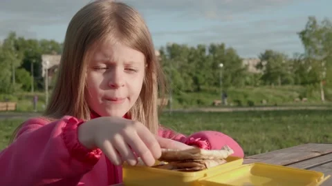Child bites sharma from yellow lunch box in outside. Stock Footage 137409909
