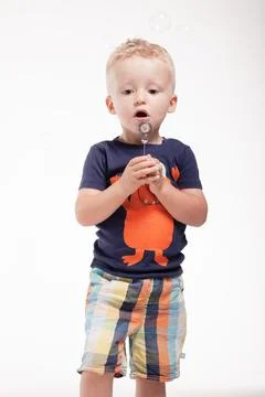 Child blowing bubbles in the studio with a plain background wearing a colorful Stock Photos
