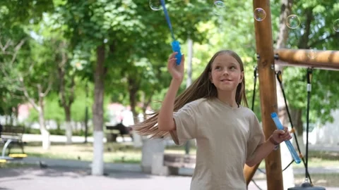 A child blows soap bubbles in the park. Girl blowing bubbles on the playground Stock Footage 302801035