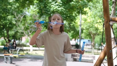 A child blows soap bubbles in the park. Girl blowing bubbles on the playground Stock Footage 302801041