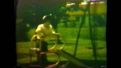 Child in bonnet and jacket plays on a slide in her backyard. 動画素材 147949136