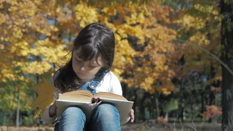 Child with a book in the park. Vídeos de archivo 98190769