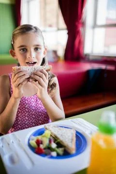 Child at booth holding triangular sandwich near mouth with salad on blue plate Foto stock