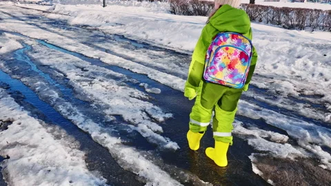 A child in boots walks through puddles of melting snow Stock Footage 256237530