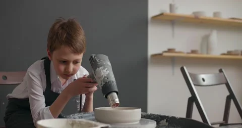 Child boy in apron is drying ceramic blank on rotating wheel at pottery studio Stock Footage 155864725