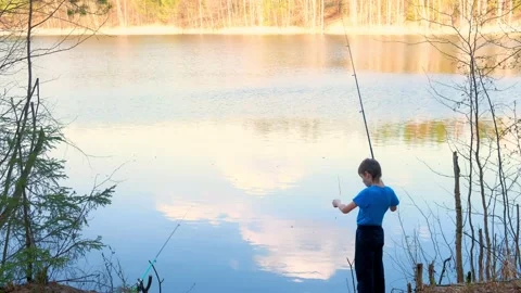Child boy is catching a fish in river using a fishing rod at sunset, back view. Stock Footage 136423717