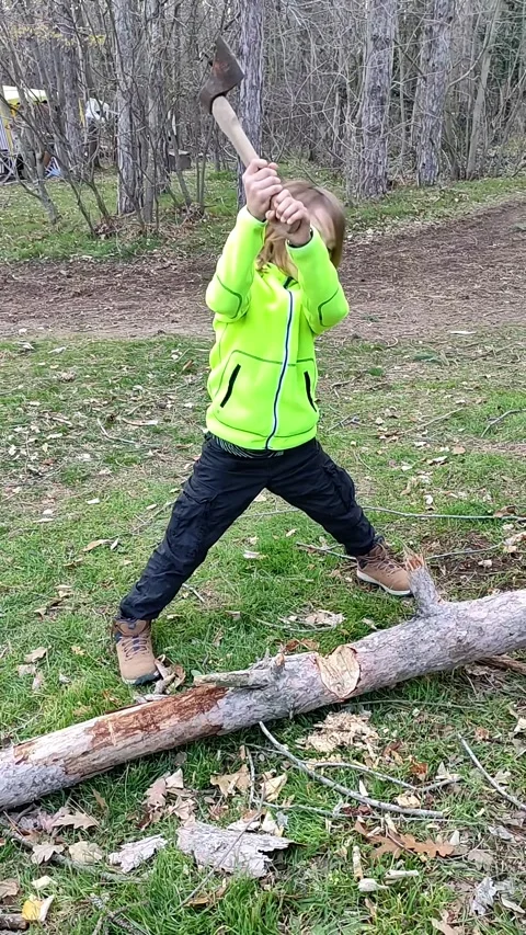 A child boy chopping a log with an axe in a forest clearing, showcasing focus Stock Footage 298019008