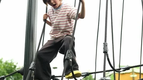 A child boy is climbing up an alpine grid in a park on a playground on a hot Stock Footage 312515273