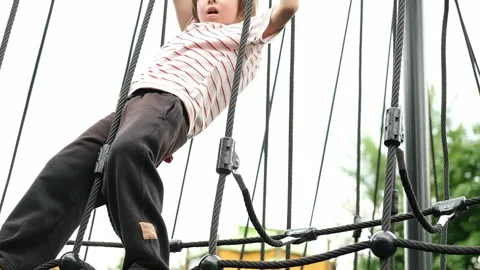 A child boy is climbing up an alpine grid in a park on a playground on a hot Stock Footage 312515296