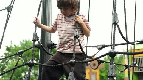 A child boy is climbing up an alpine grid in a park on a playground on a hot Stock Footage 312515354