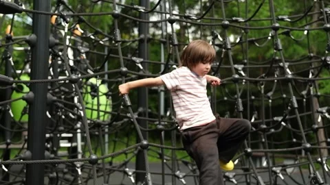 A child boy is climbing up an alpine grid in a park on a playground on a hot Stock Footage 312515407